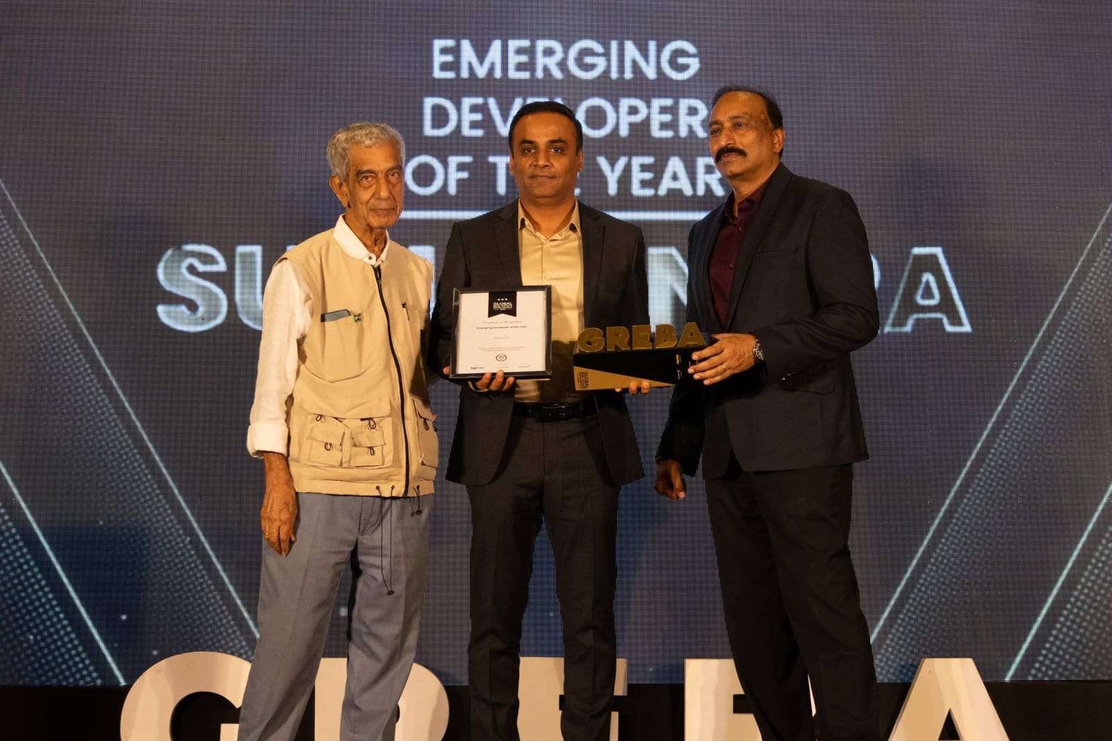 Suyug Infra receiving the Emerging Developer of the Year award at the Global Real Estate Brand Awards, holding the certificate and the GREBA trophy on stage