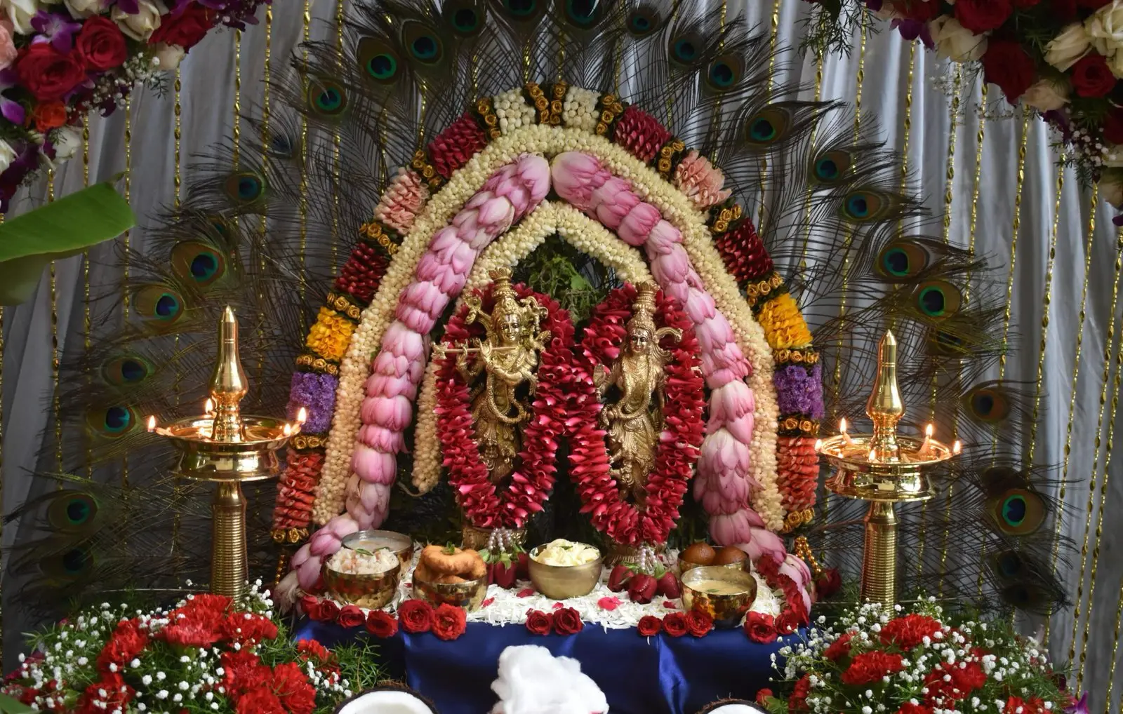 The shrine built for the day: gilded idols under an arch of lotus buds and rose garlands, brass lamps lit on either side.
