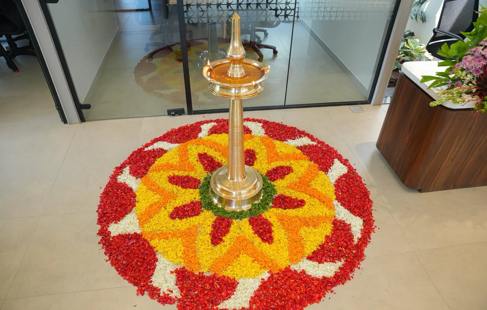 The pookalam laid out on the lobby floor in red, orange and white petals, the brass nilavilakku standing at its centre.